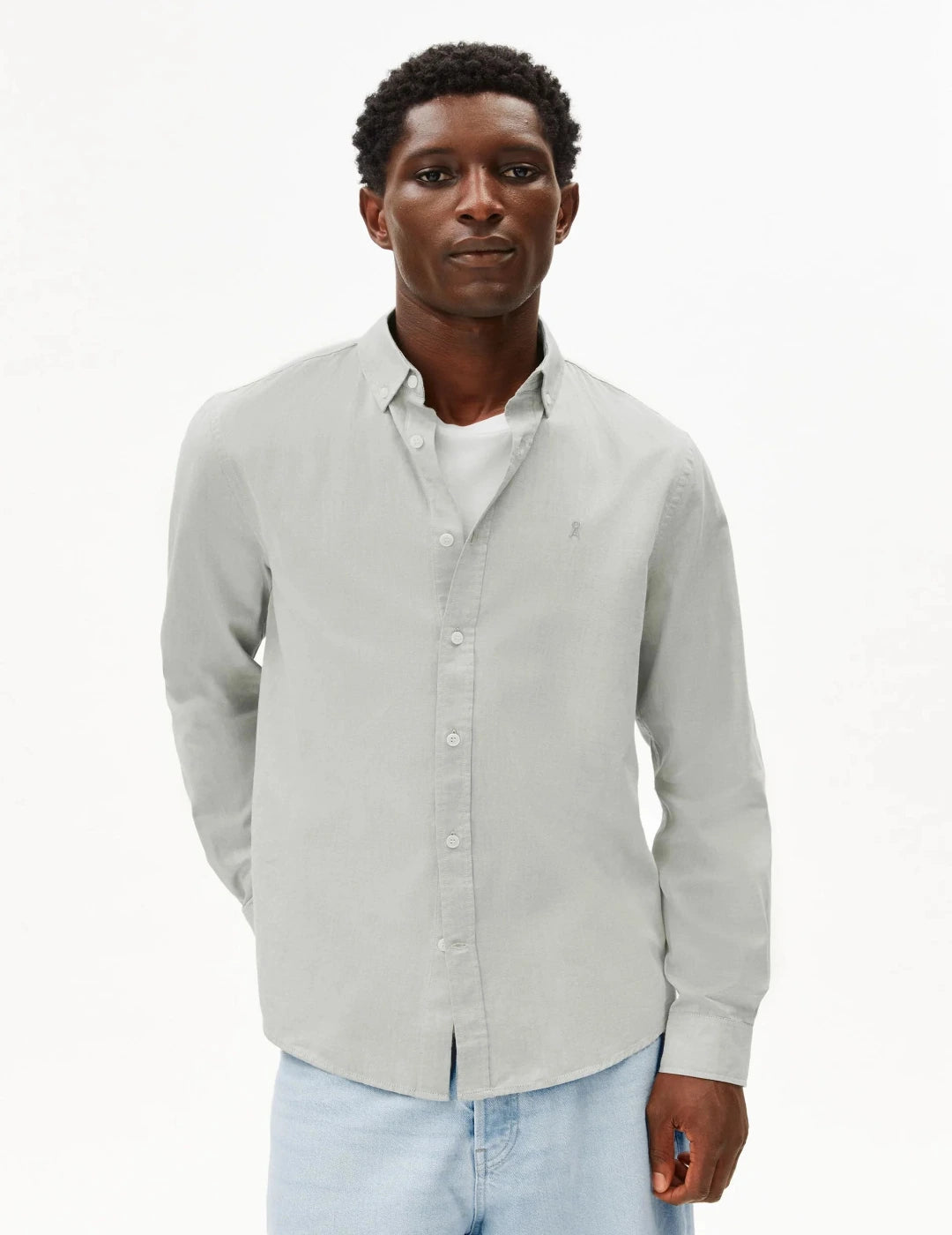Man wearing a light gray button-up shirt over a white shirt with light blue jeans on a white background