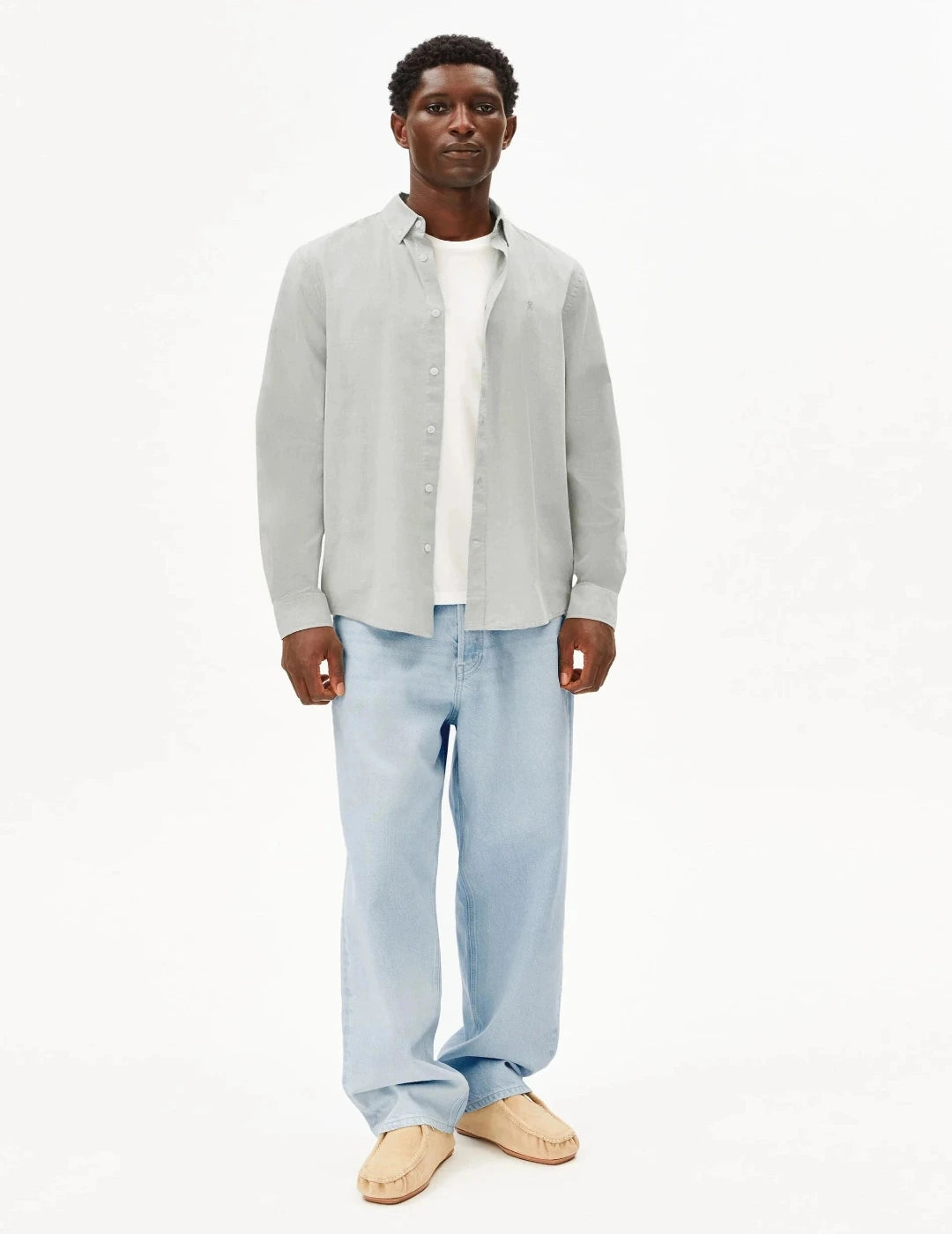 Man wearing a light gray shirt over a white collared shirt with light blue jeans on a white background