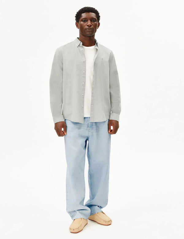 Man wearing a light gray shirt over a white collared shirt with light blue jeans on a white background