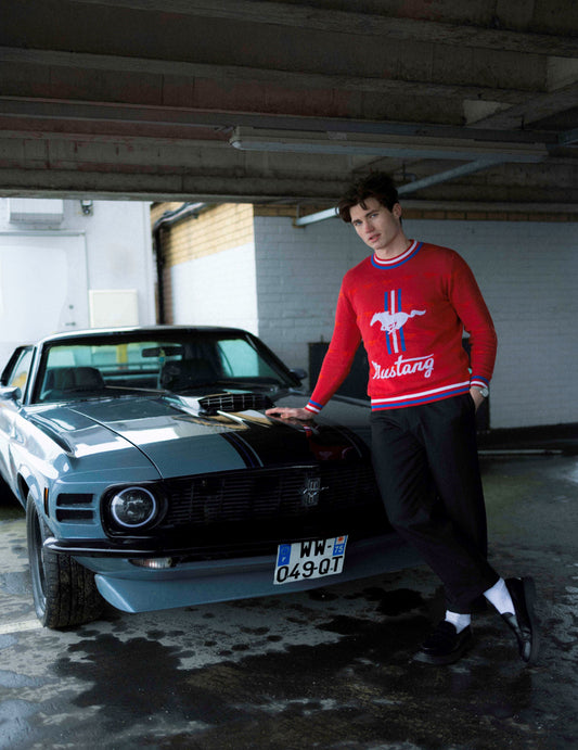 Man wearing red Ford Mustang Knit jumper leaning against a Ford Mustang car