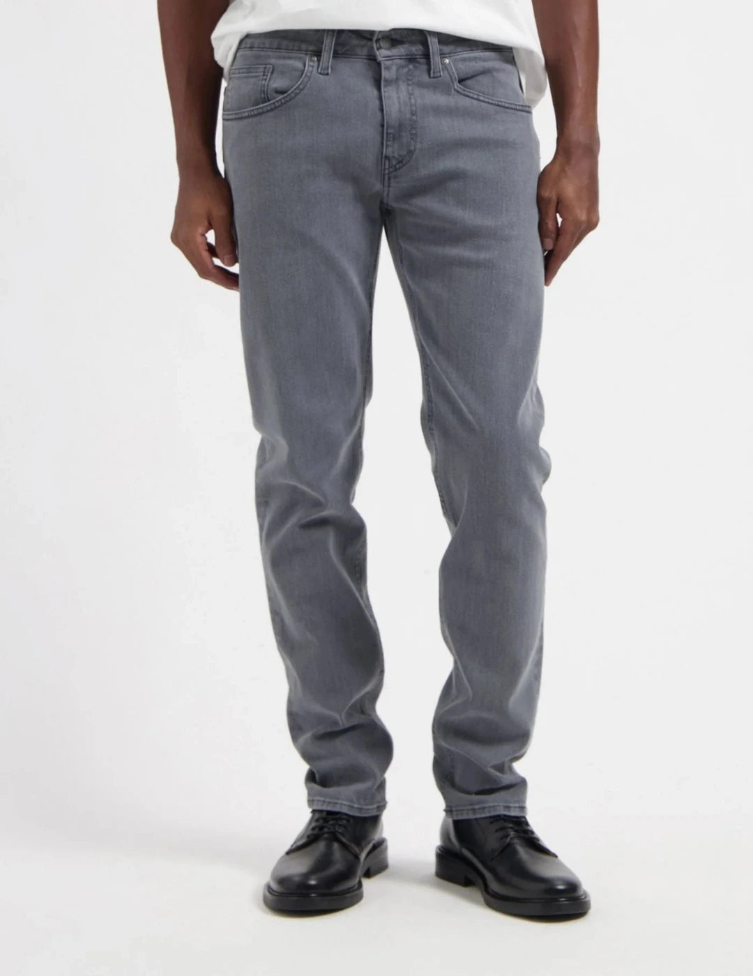 A person wearing slim-fit gray denim jeans with a white shirt and black leather shoes, shown from the waist down against a plain white studio background.